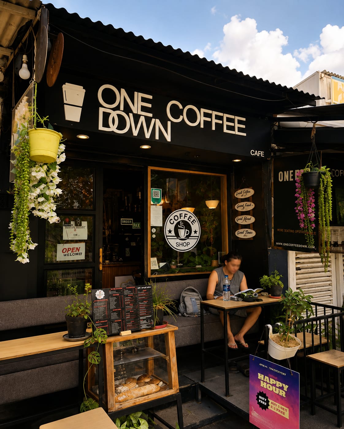 One Coffee Down storefront on Sunset Road with hanging plants and a guest reading over coffee